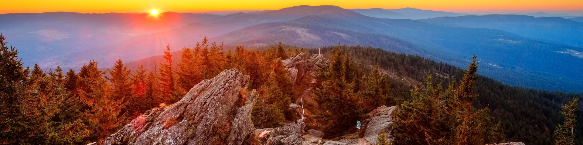 A mountainous landscape with a sunset, rocky terrain, and a trail marked by signs.