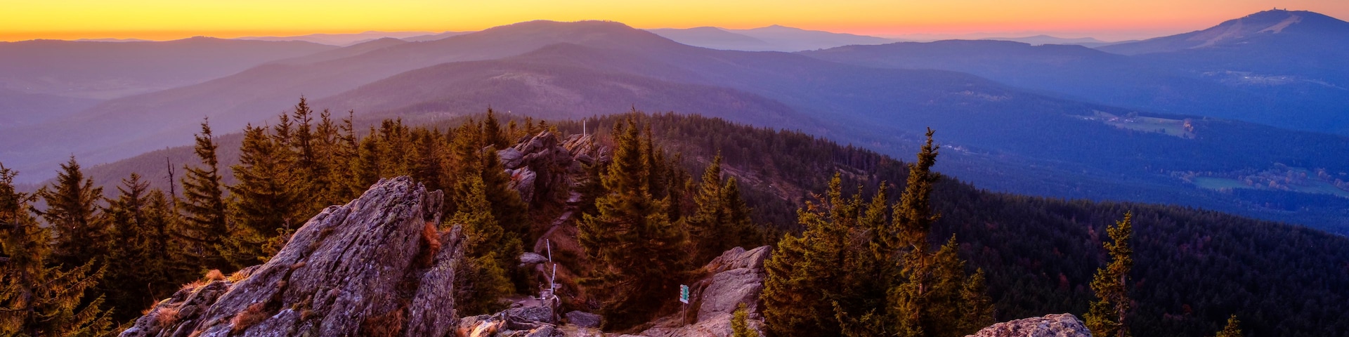 Paisagem montanhosa com florestas densas e terreno rochoso ao pôr do sol.