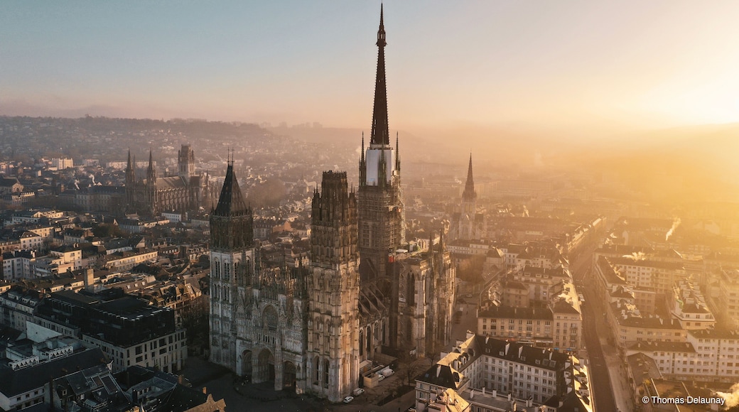 Une cathédrale dotée d’une haute flèche, entourée d’un paysage urbain composé de différents bâtiments et surplombée d’un ciel dégagé.