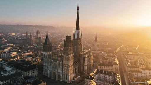 Un duomo con una guglia alta, circondato da un panorama urbano con diversi edifici e un cielo sereno.