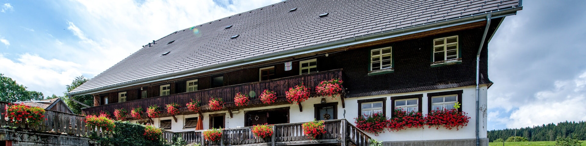 A traditional chalet with a steep roof, wooden balconies with flower boxes, and a stone wall in the foreground.