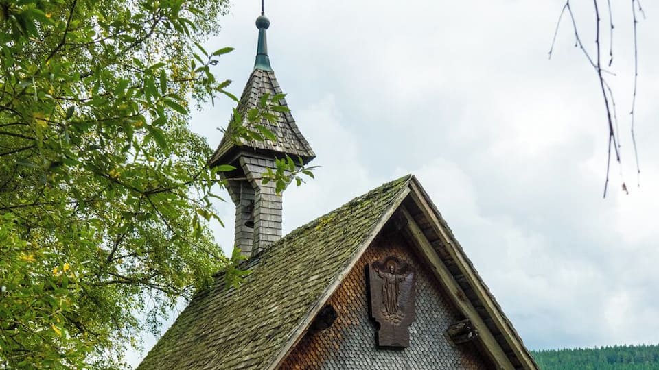 A small church with a steeply pitched roof, a weather vane, and a cross on top.
