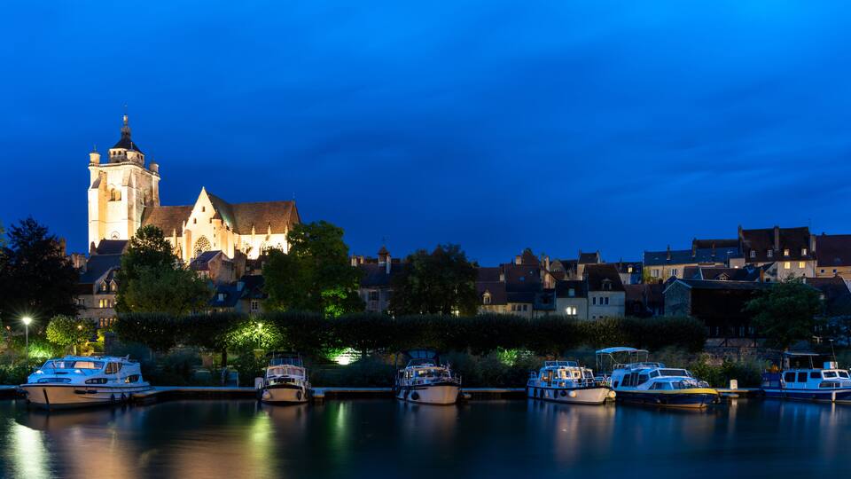 A historic church with a prominent tower, surrounded by residential buildings and a calm water body with boats.