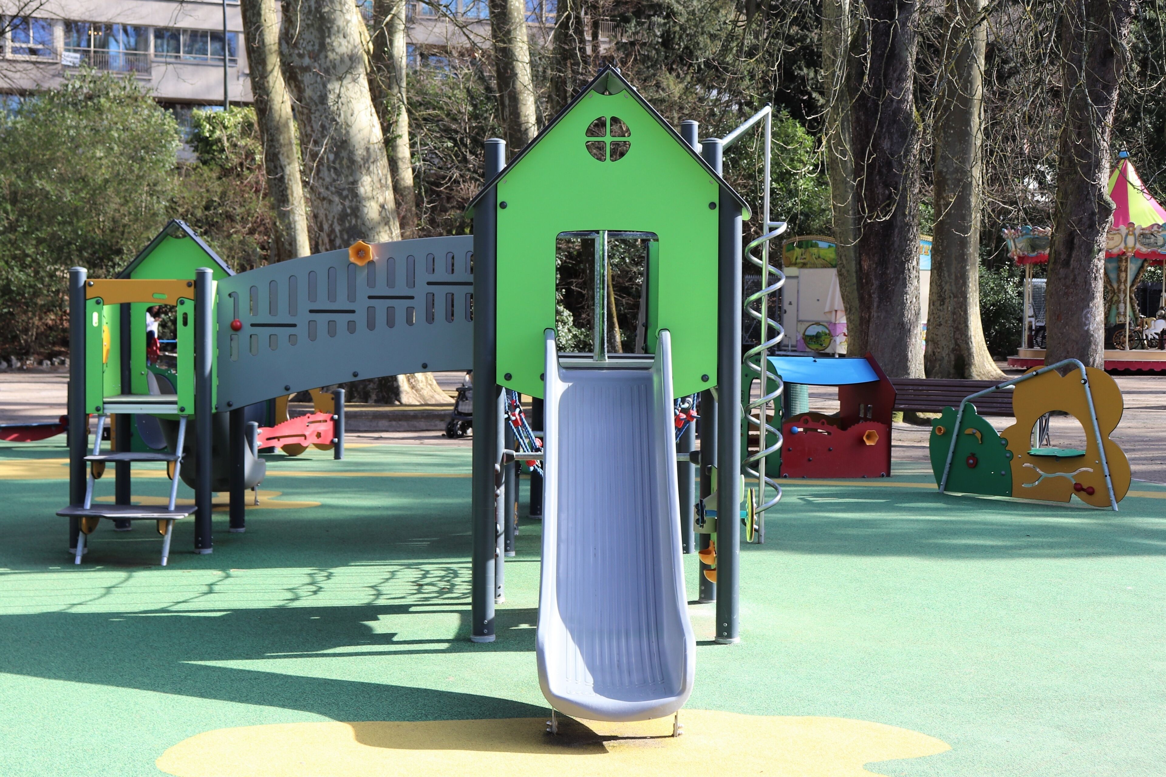 Un parque infantil con un tobogán, estructuras para escalar y una casita con forma de casa.