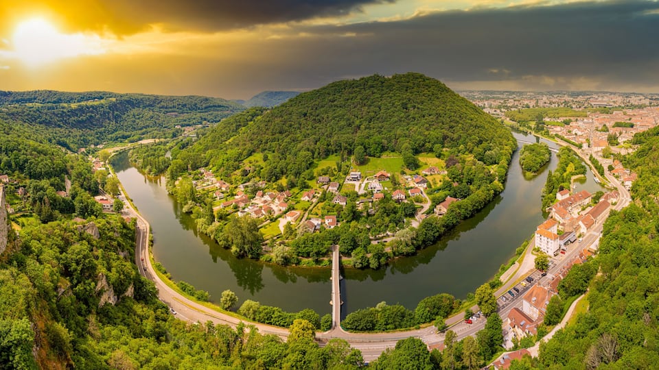 A river winding through a town surrounded by hills, with a prominent hill in the center.