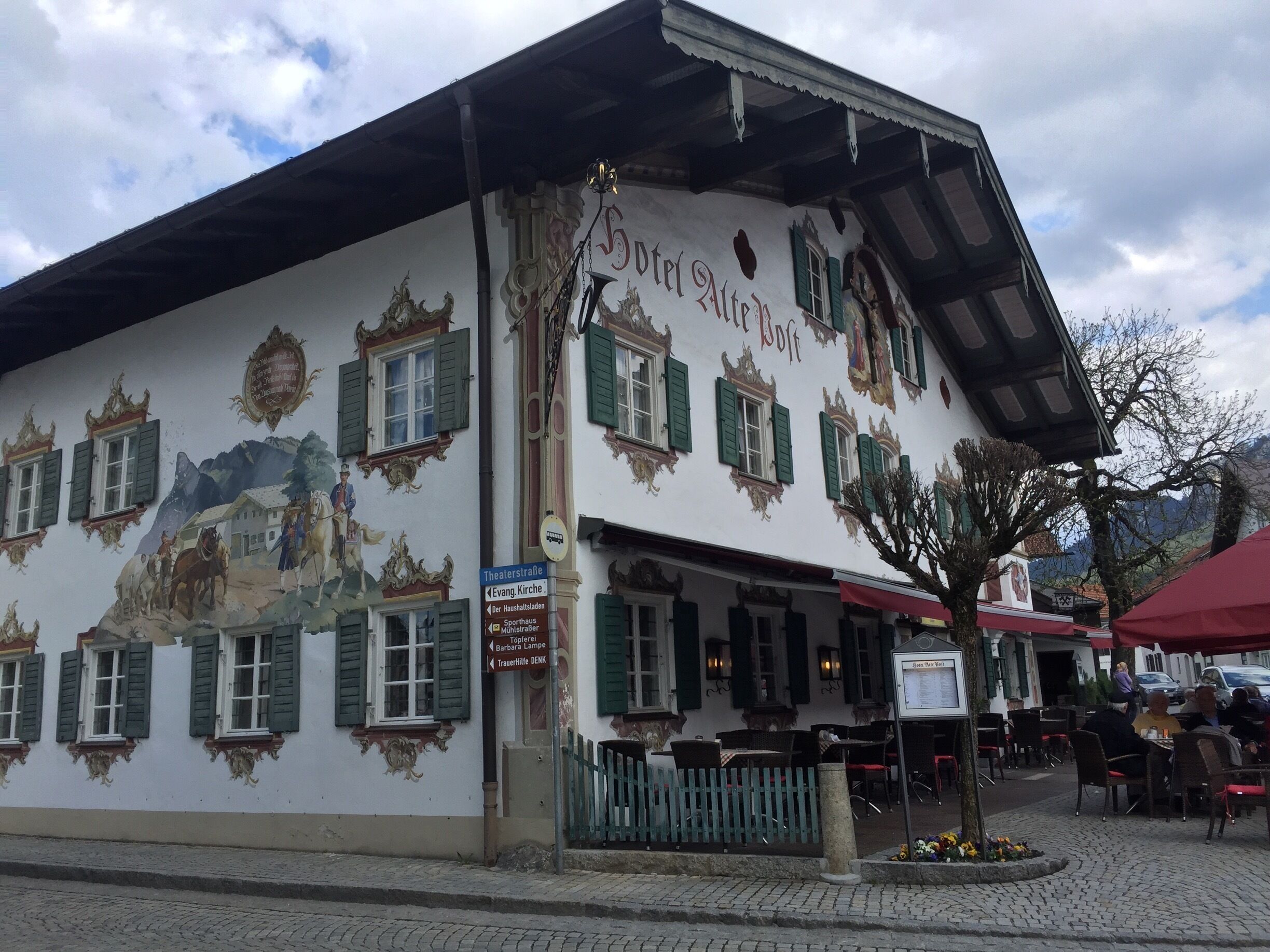 A traditional building with a mural, green shutters, and outdoor seating.