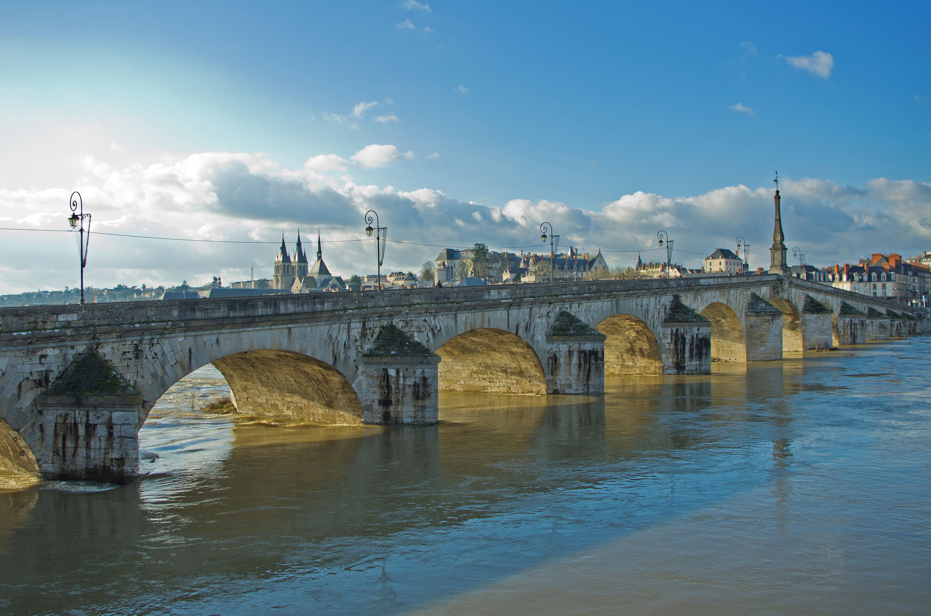 A historic stone bridge with multiple arches over a river, with buildings and a church in the background.