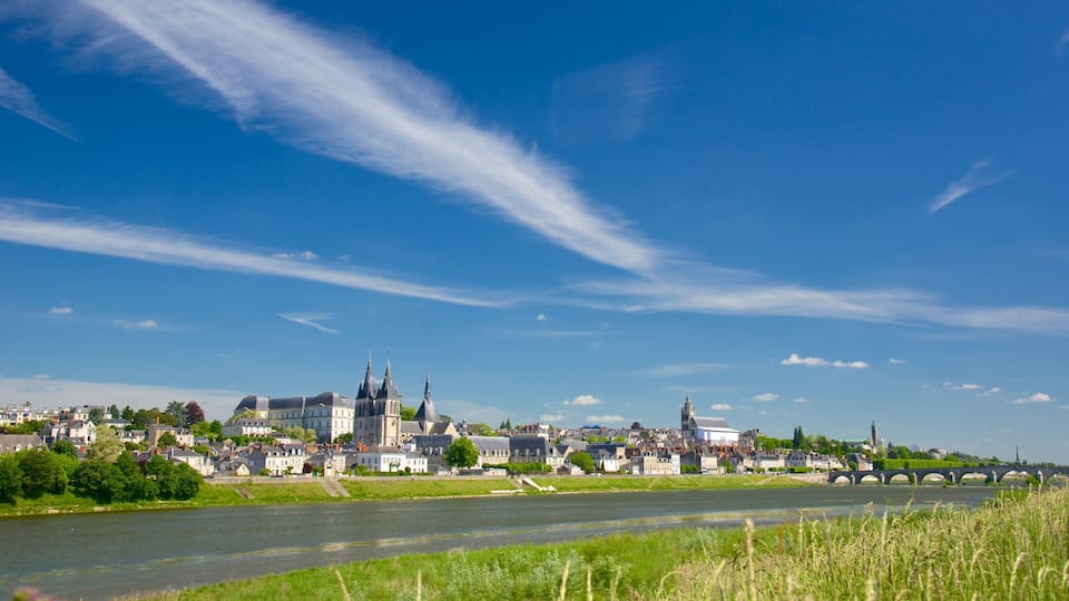 A river with a bridge, a town with historic buildings, and a clear blue sky.