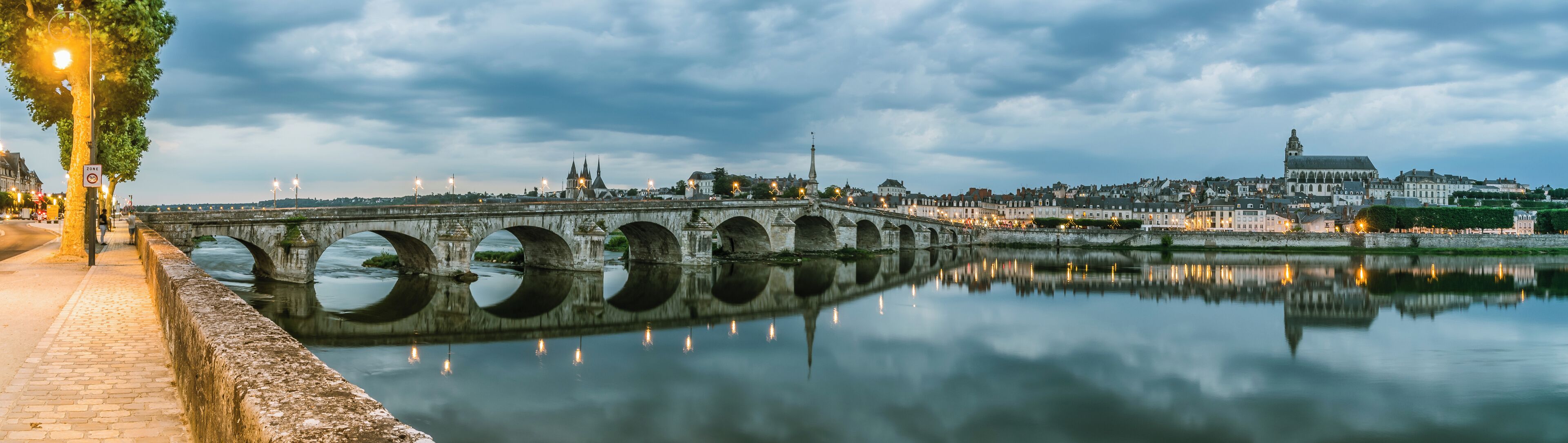 A stone bridge over a calm river, reflecting city lights and buildings.