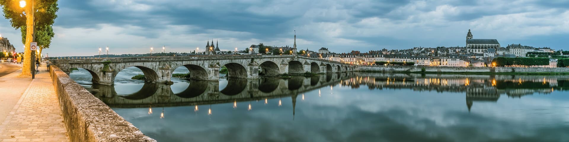 A stone bridge over a calm river, reflecting city lights and buildings.