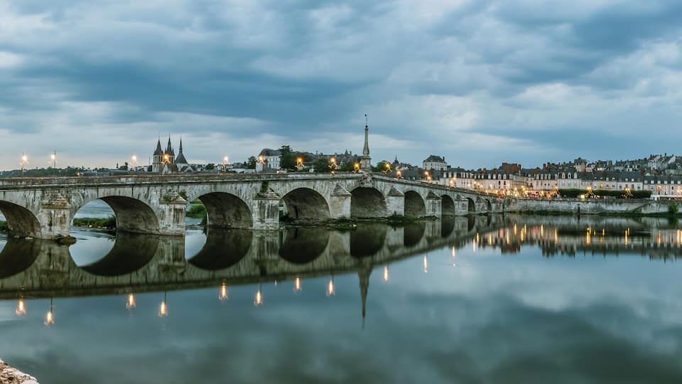 A stone bridge over a calm river, reflecting city lights and buildings.