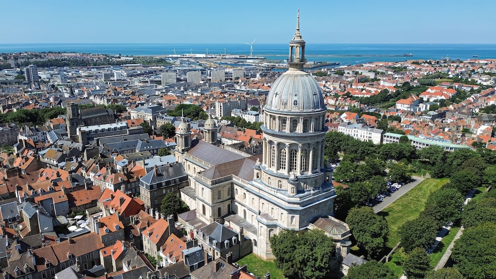 Un paysage urbain côtier avec une église imposante, caractérisée par un grand dôme et un clocher.