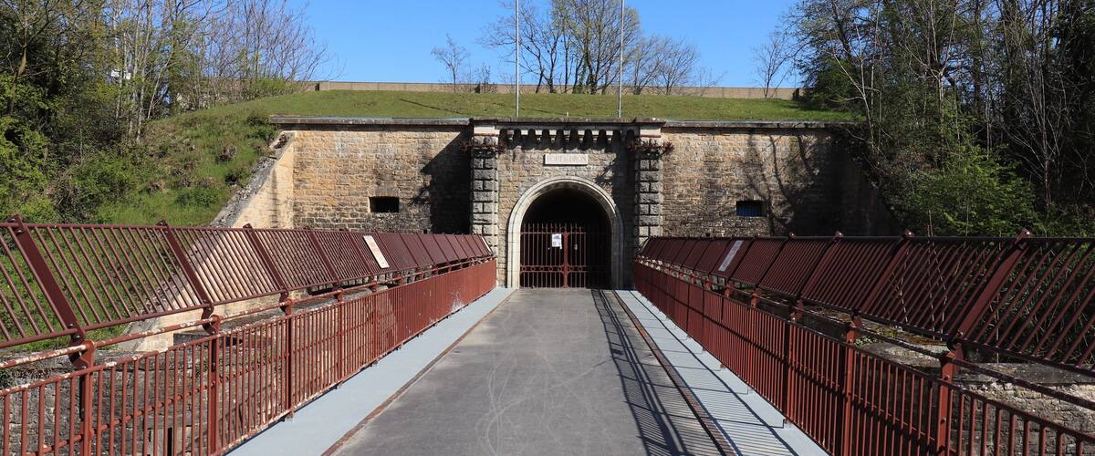 A stone bridge with metal railings leading to a tunnel entrance.