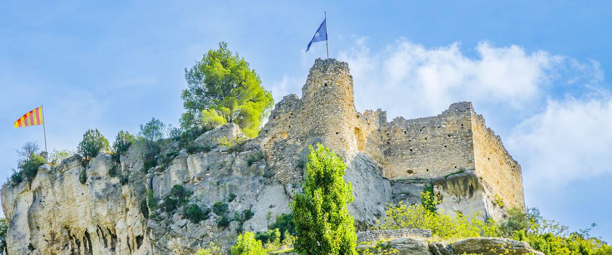 A historic stone castle atop a rocky cliff with two flags.