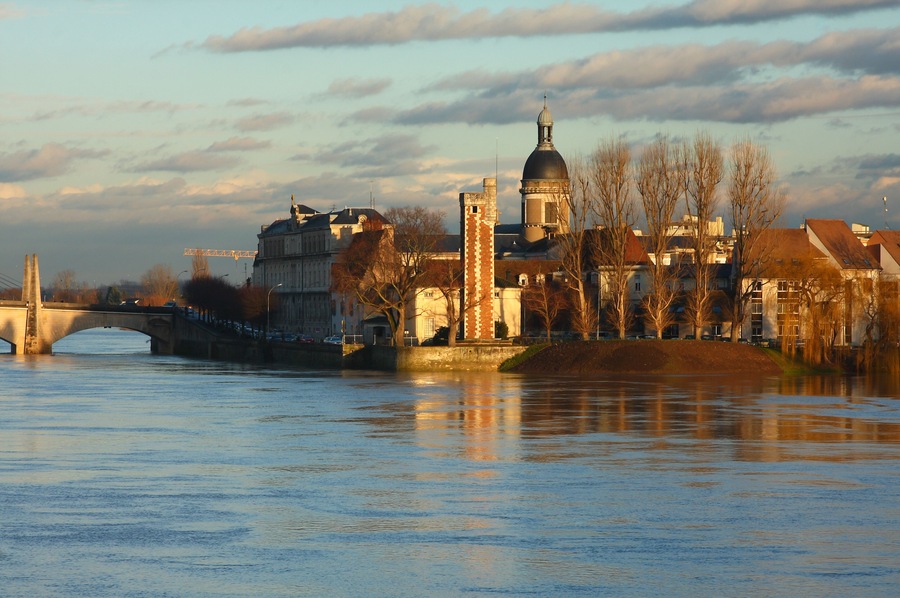 Une rivière traversée par un pont, avec une tour et des bâtiments en arrière-plan.