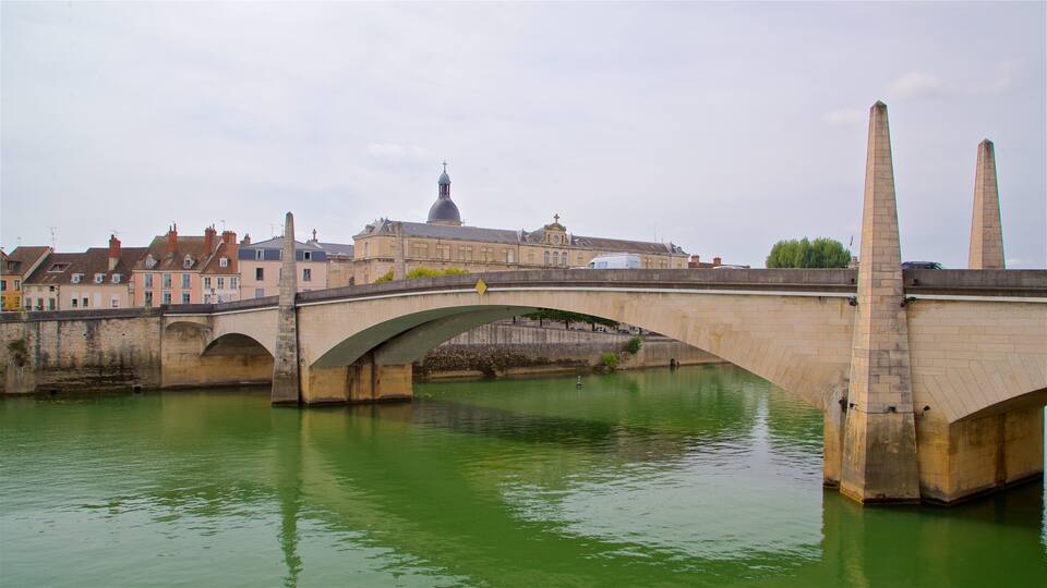 A stone bridge over a green river with buildings and a church in the background.