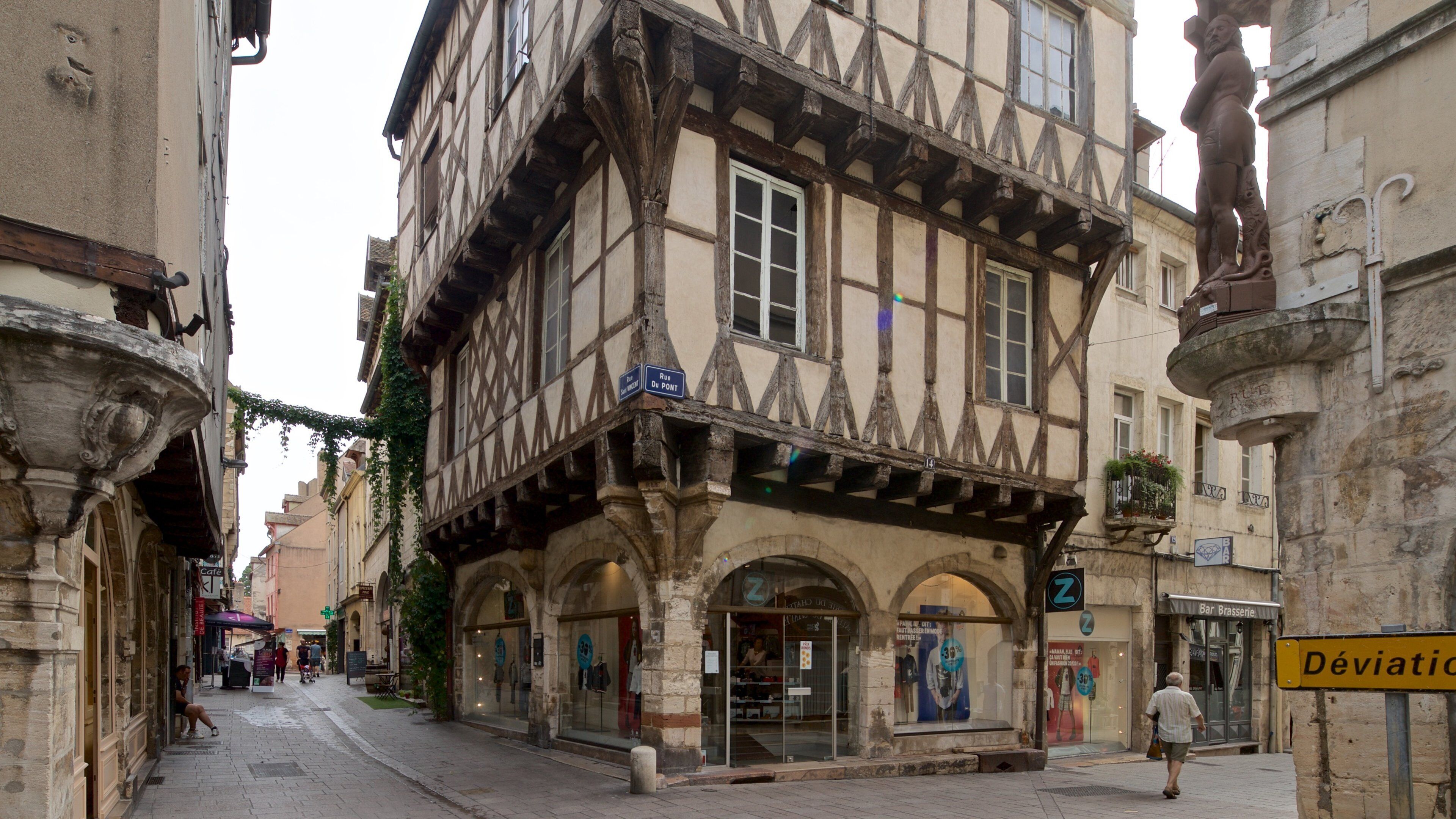 A narrow medieval street with half-timbered buildings, a café, and a bar.