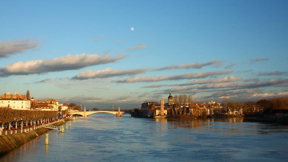 A river with a bridge, a town with historic buildings, and a clear sky with clouds.