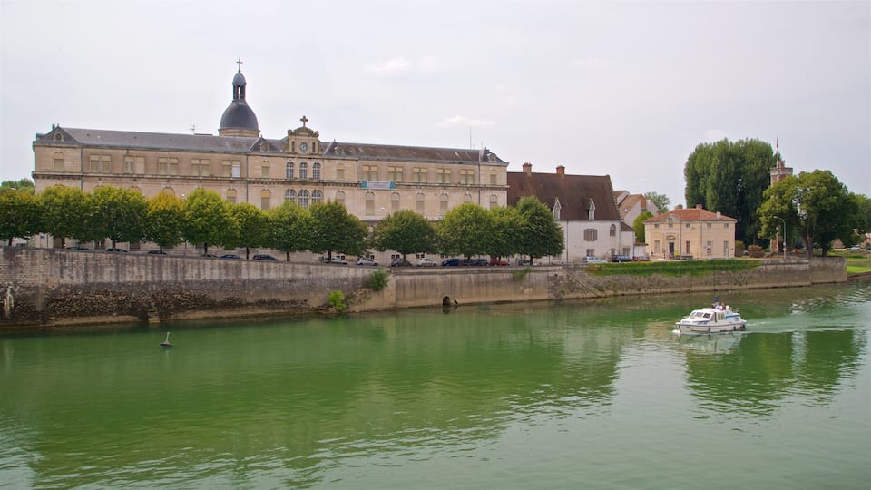 A historic building with a prominent dome and clock tower, a river with a boat, and a tree-lined embankment.