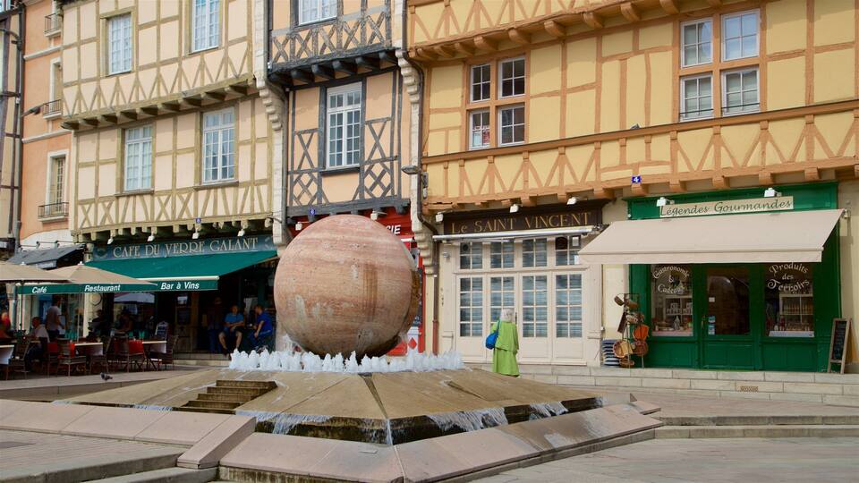 A traditional European town square with a large stone fountain, half-timbered buildings, and various shops.