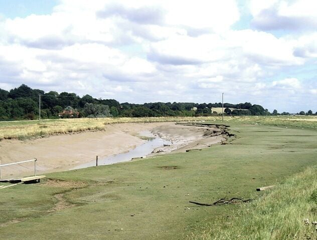A coastal landscape with a sandy beach, grassy areas, and a distant building.