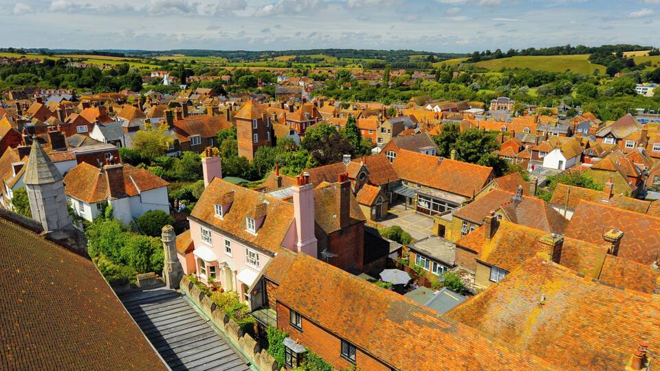 A historic town with red-roofed buildings, cobblestone streets, and green fields in the background.