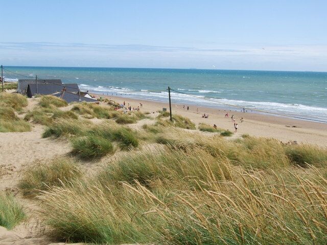 Una playa con dunas, algunas personas y un edificio al fondo.