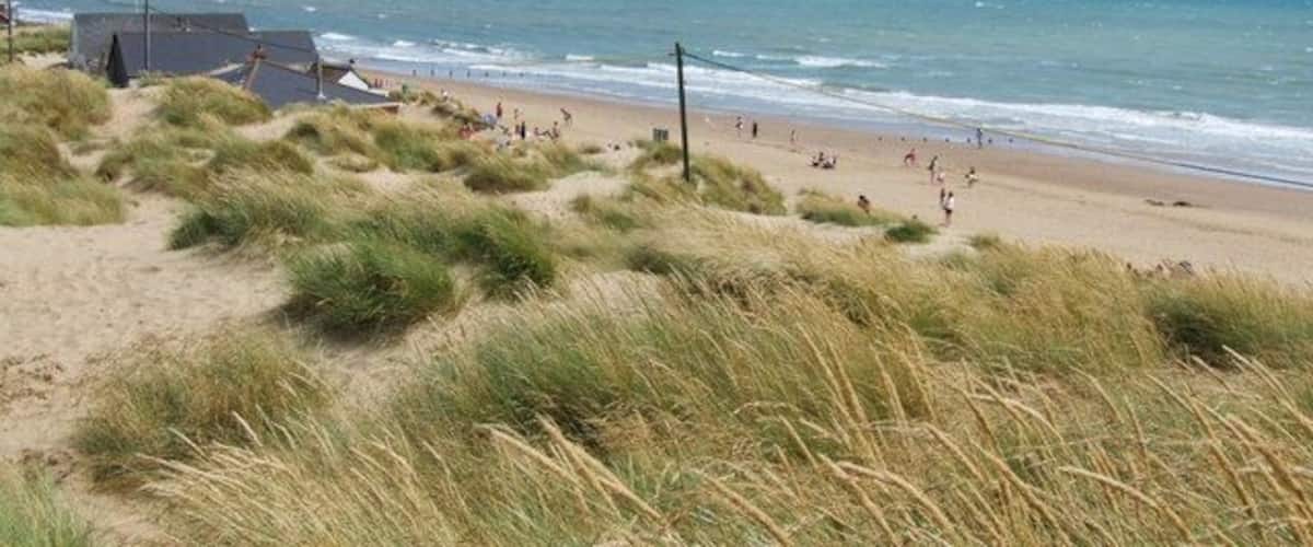 A beach with dunes, a few people, and a building in the background.