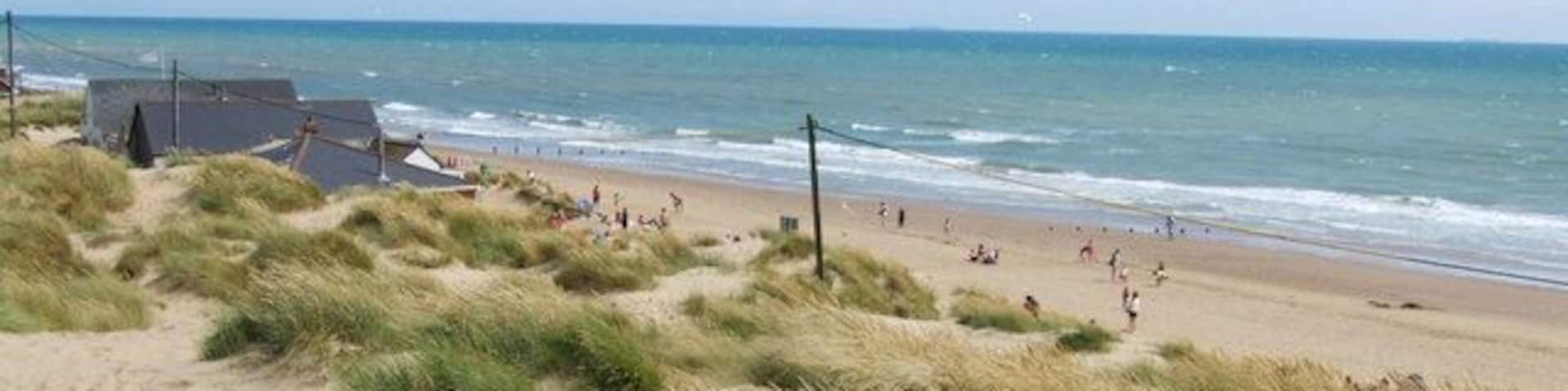 A beach with dunes, a few people, and a building in the background.
