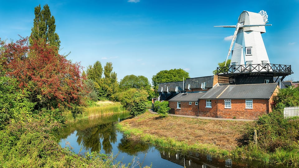 A traditional windmill, a river, and surrounding greenery.