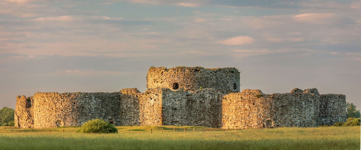 A medieval stone castle with multiple towers and walls, surrounded by a grassy field.