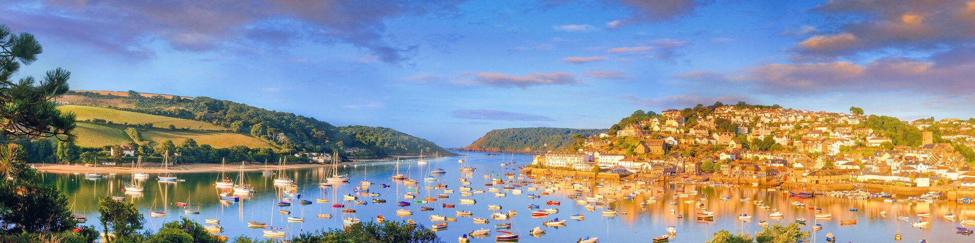 A coastal town with a harbor filled with boats, surrounded by hills and a clear sky.