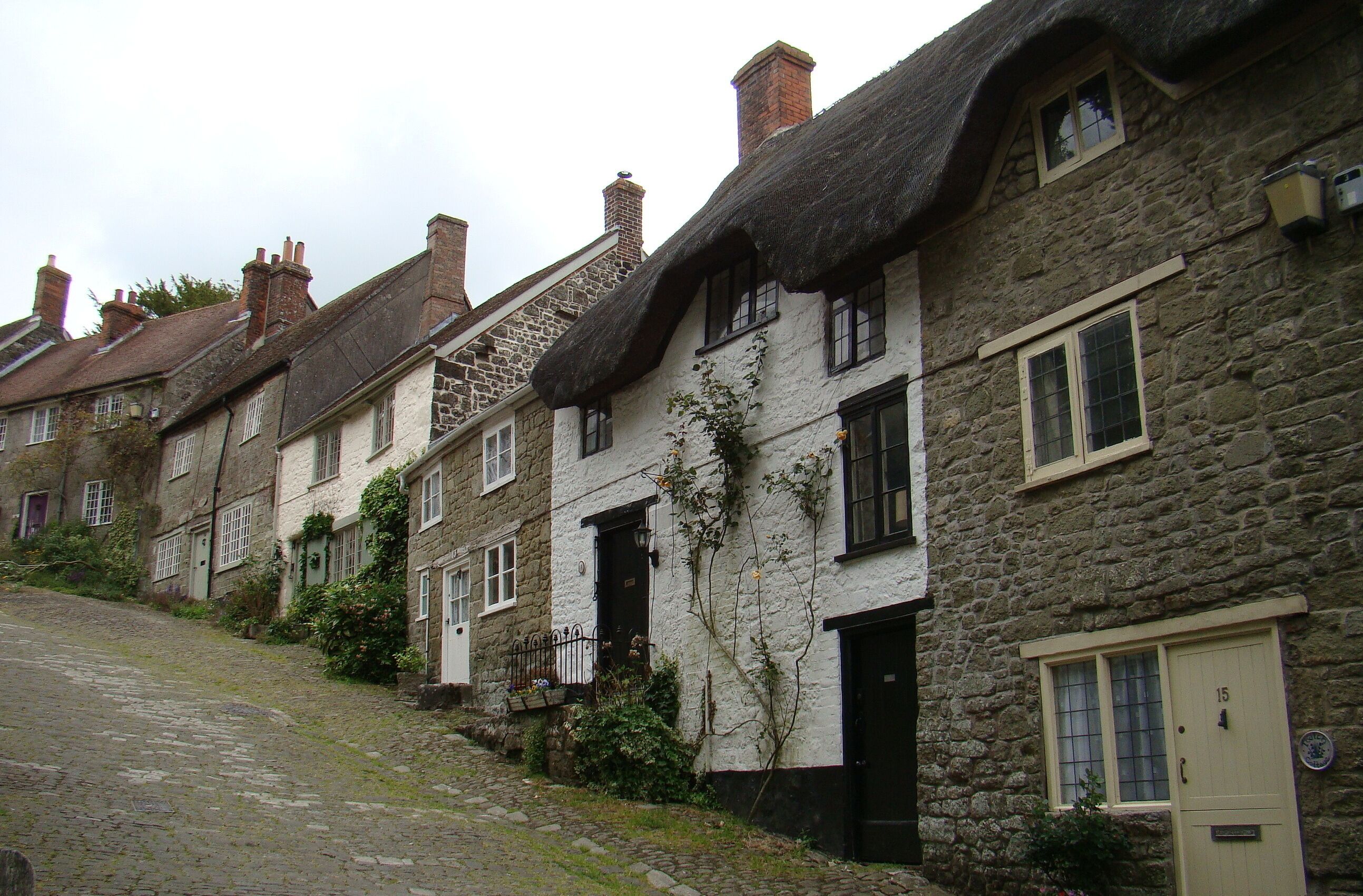 A row of stone houses with thatched roofs and a cobblestone street.