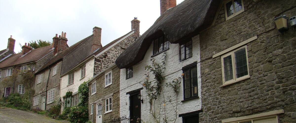 A row of stone houses with thatched roofs and a cobblestone street.