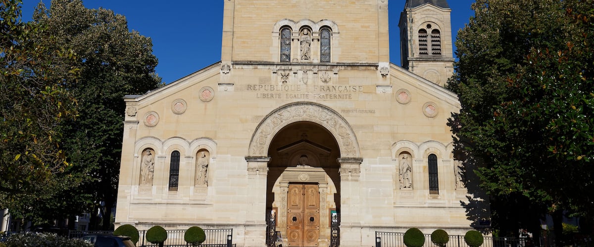 A historic building with a prominent archway, a clock tower, and statues.