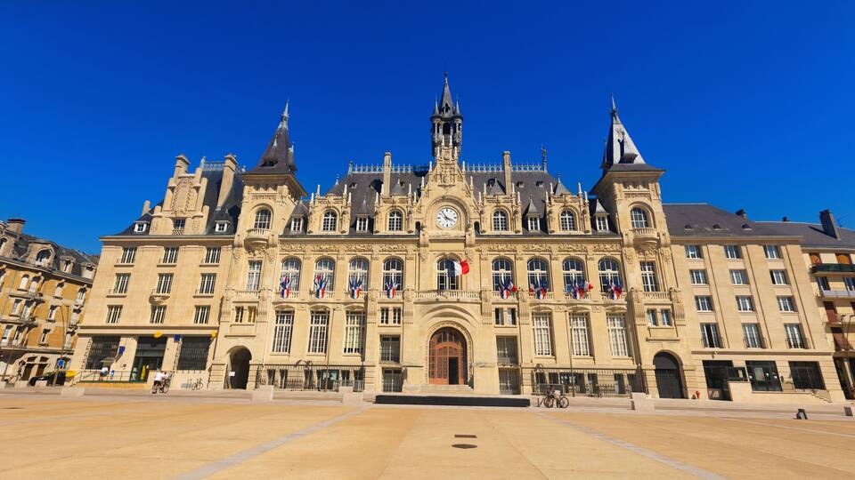 A historic building with ornate architecture, a large clock, and flags.