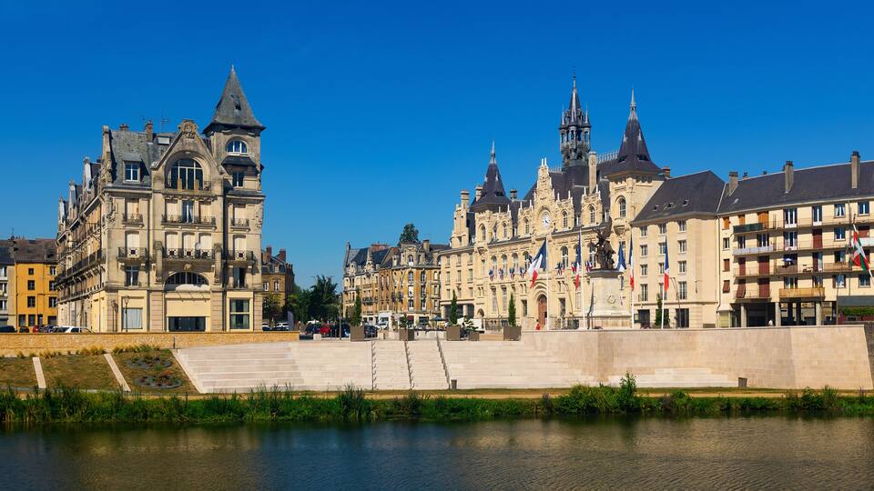 A riverside view of historic buildings with a prominent tower and flags.
