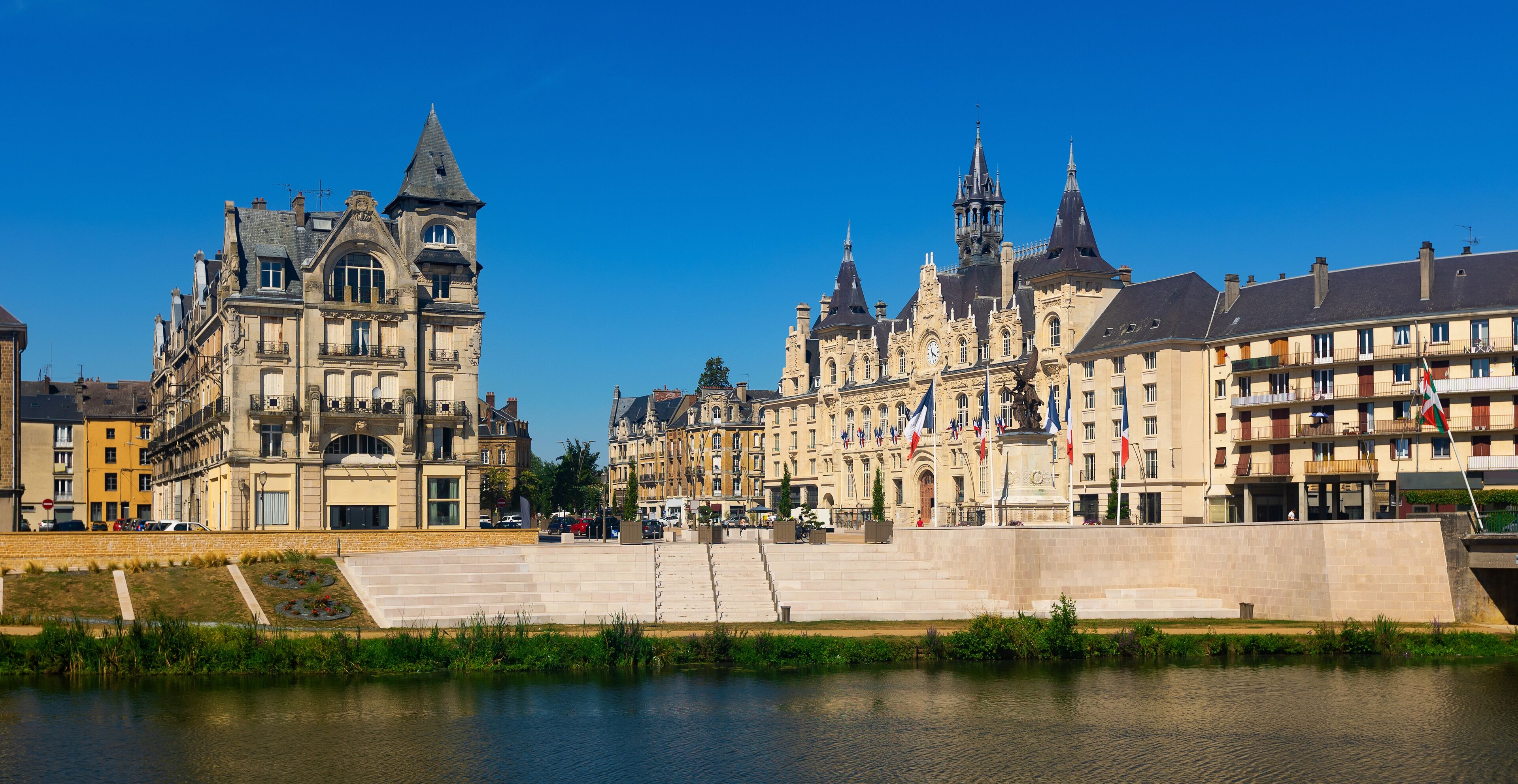 A riverside view of historic buildings with a prominent tower and flags.