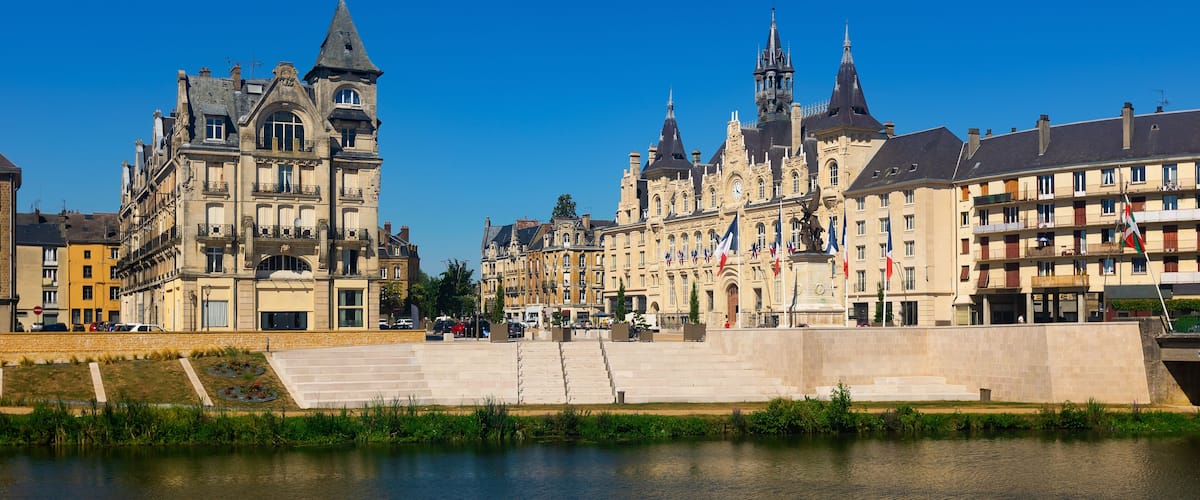 A riverside view of historic buildings with a prominent tower and flags.