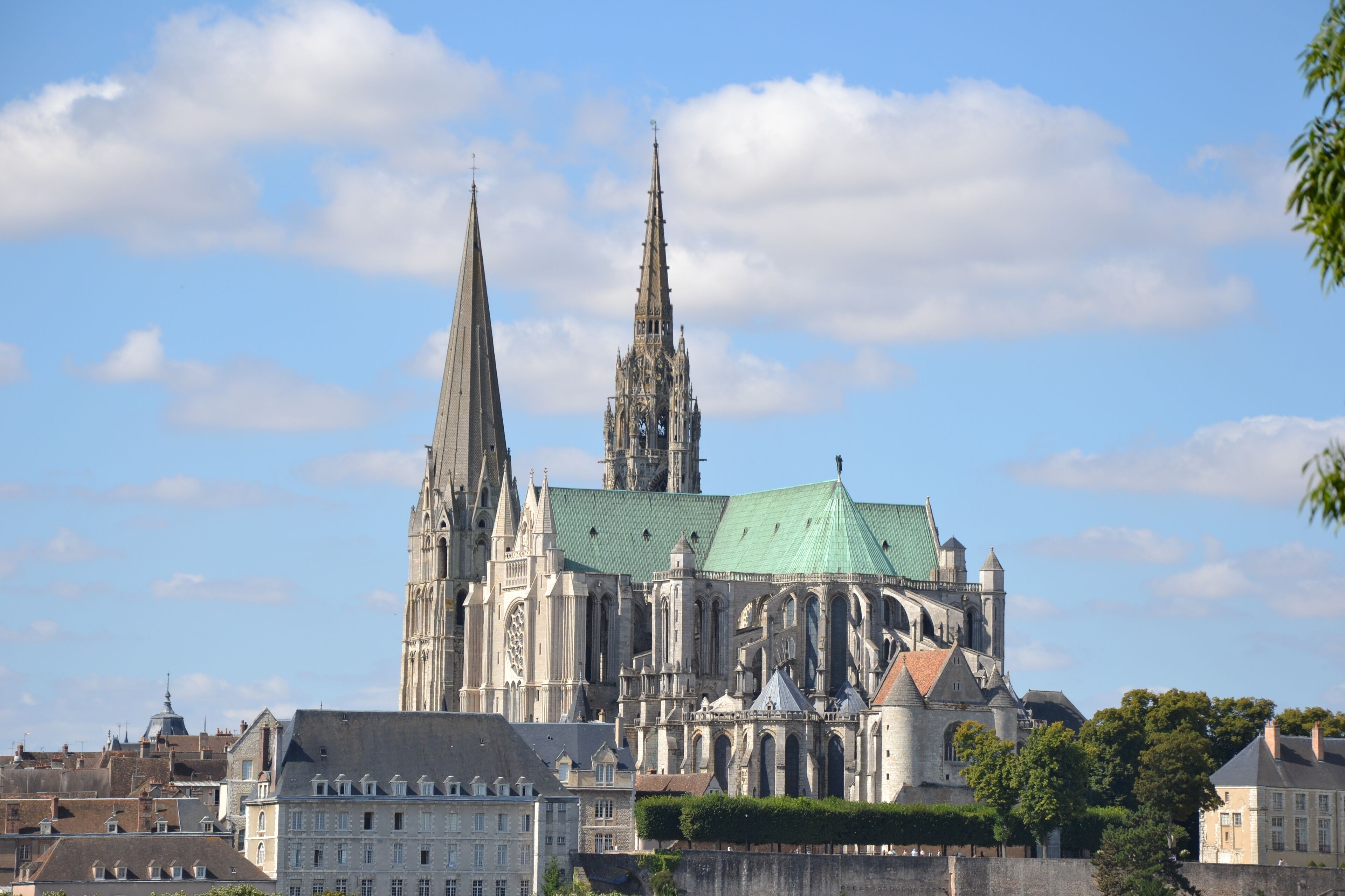 A historic cathedral with twin spires and a green roof, surrounded by urban buildings and trees.