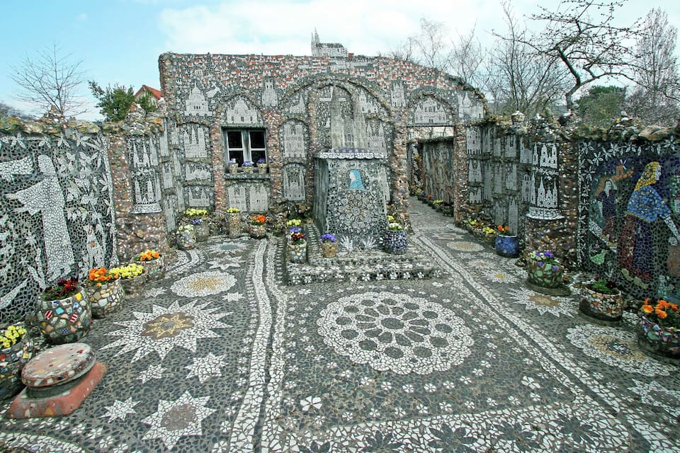 Une cour dallée de mosaïques, avec une fontaine centrale, entourée de murs en pierre et de jardinières.