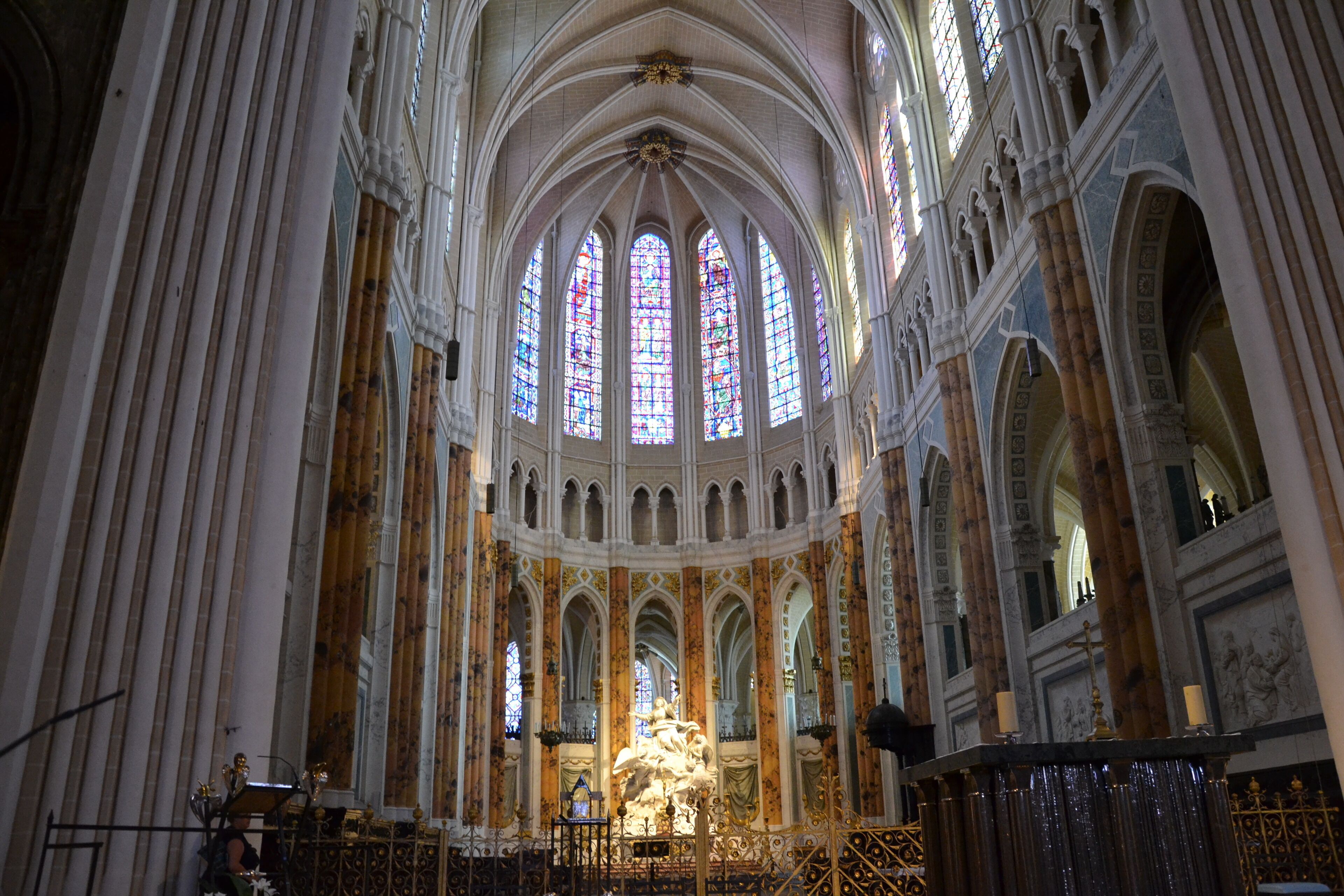 A cathedral interior with high vaulted ceilings, stained glass windows, and a central altar.