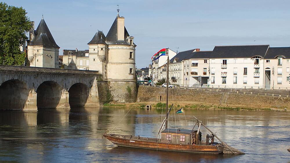 Une rivière avec un pont, un château et un bateau.