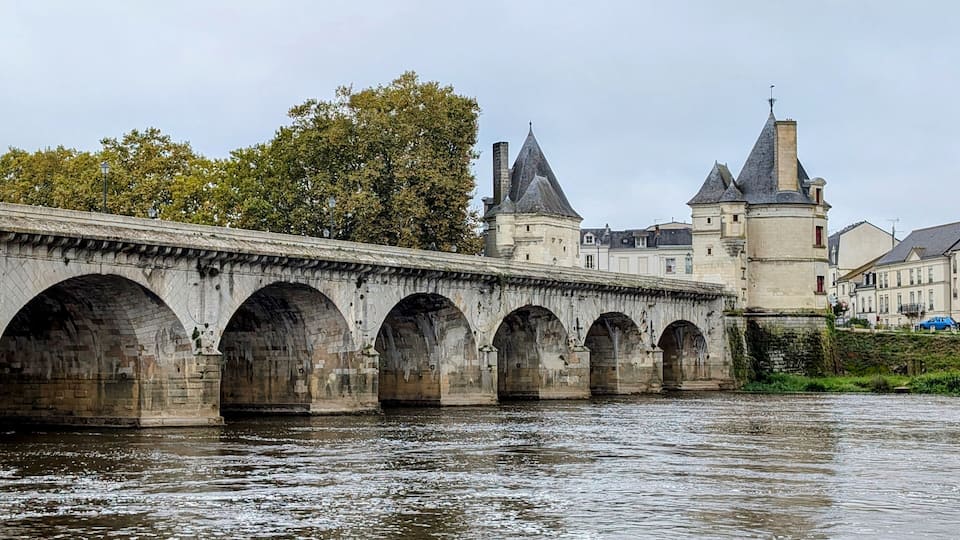 A stone bridge with multiple arches over a river, leading to a castle with towers.