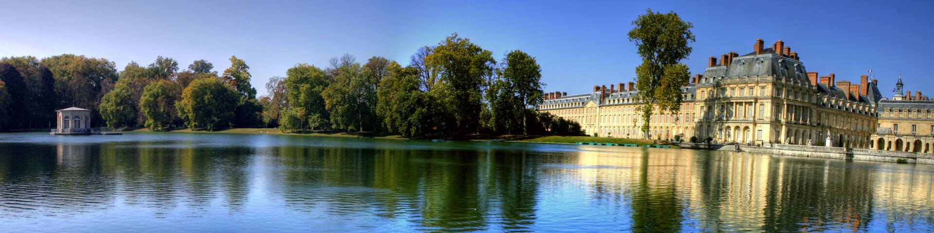 A calm lake with a historic building and a gazebo on the shore.