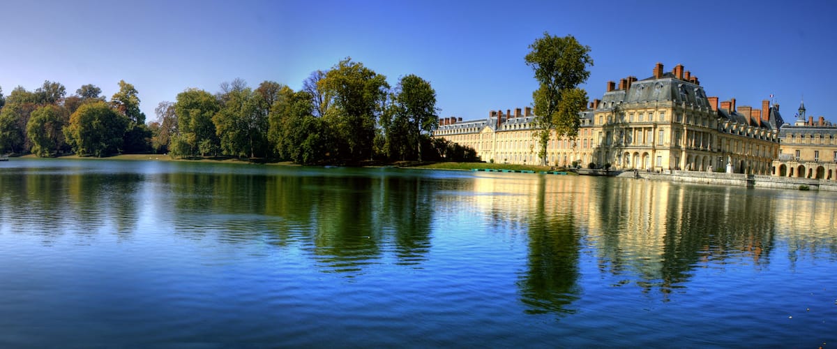A calm lake with a historic building and a gazebo on the shore.