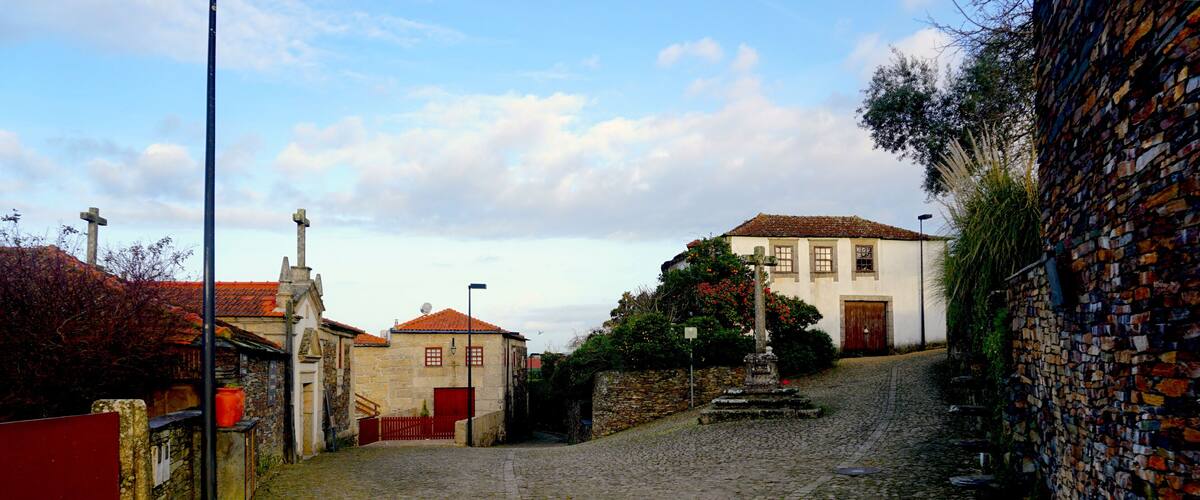 A cobblestone street with historic buildings, a stone wall, and a cross.