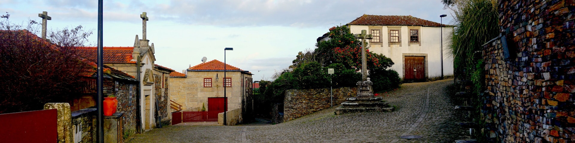 A cobblestone street with historic buildings, a stone wall, and a cross.