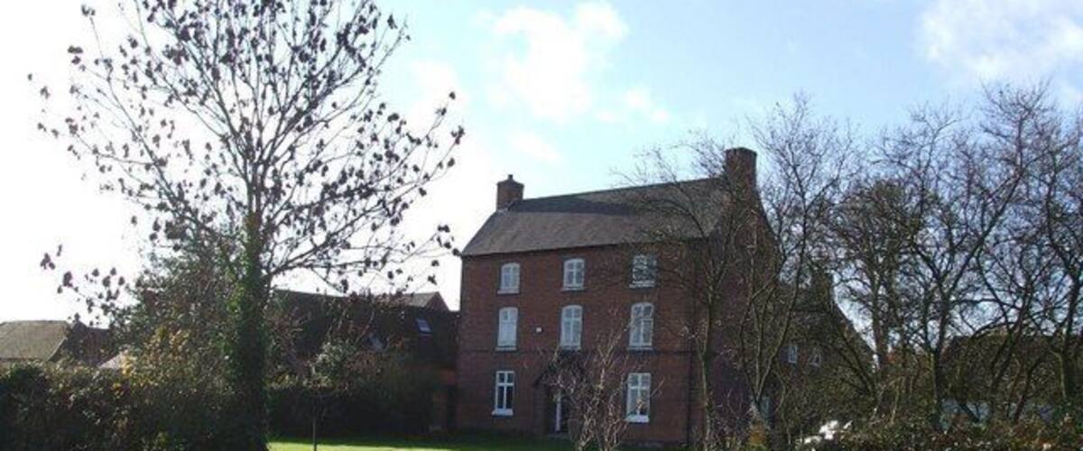 A red brick building with a grassy lawn and a tree in the foreground.