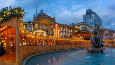 Um edifício histórico com arquitetura elaborada, uma fonte com uma estátua e luzes festivas.